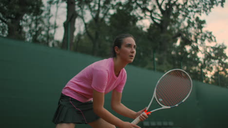 A-young-woman-trains-on-a-hard-surface-tennis-court-at-sunset-the-ready-position.